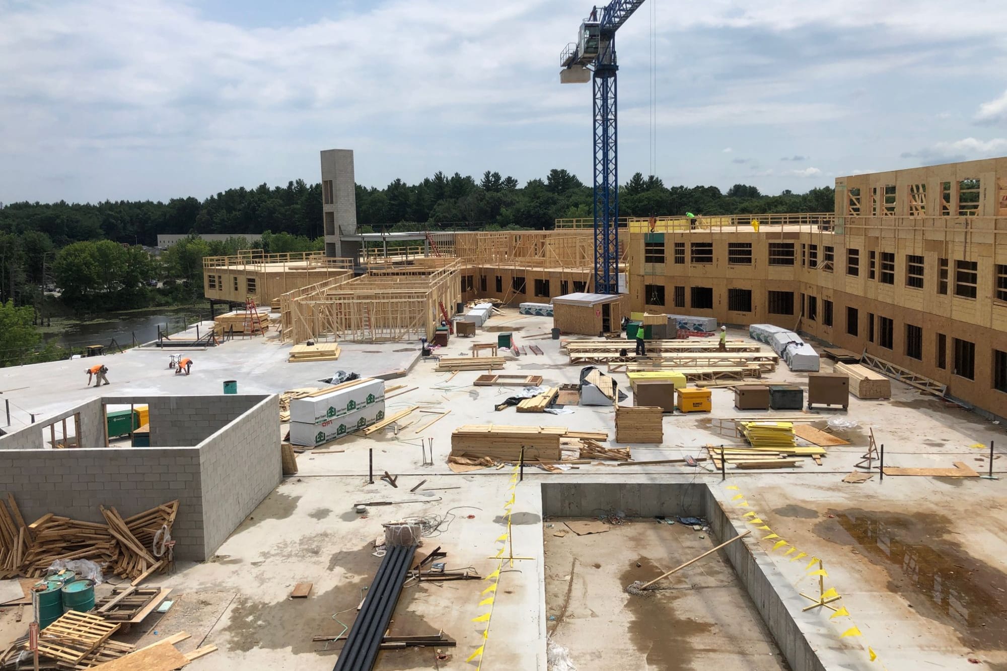 Tower crane over a podium deck, with wood-frame walls going up and lumber staged across the slab